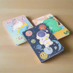 Three colorful notebooks with cartoon character designs on a white background
