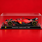 A red Ferrari SF-23 Formula 1 car display model inside a clear acrylic case on a black base, photographed against a solid red background. The base reads 'Ferrari SF-23 - Charles Leclerc - 2023' with the Ferrari shield logo on the left.