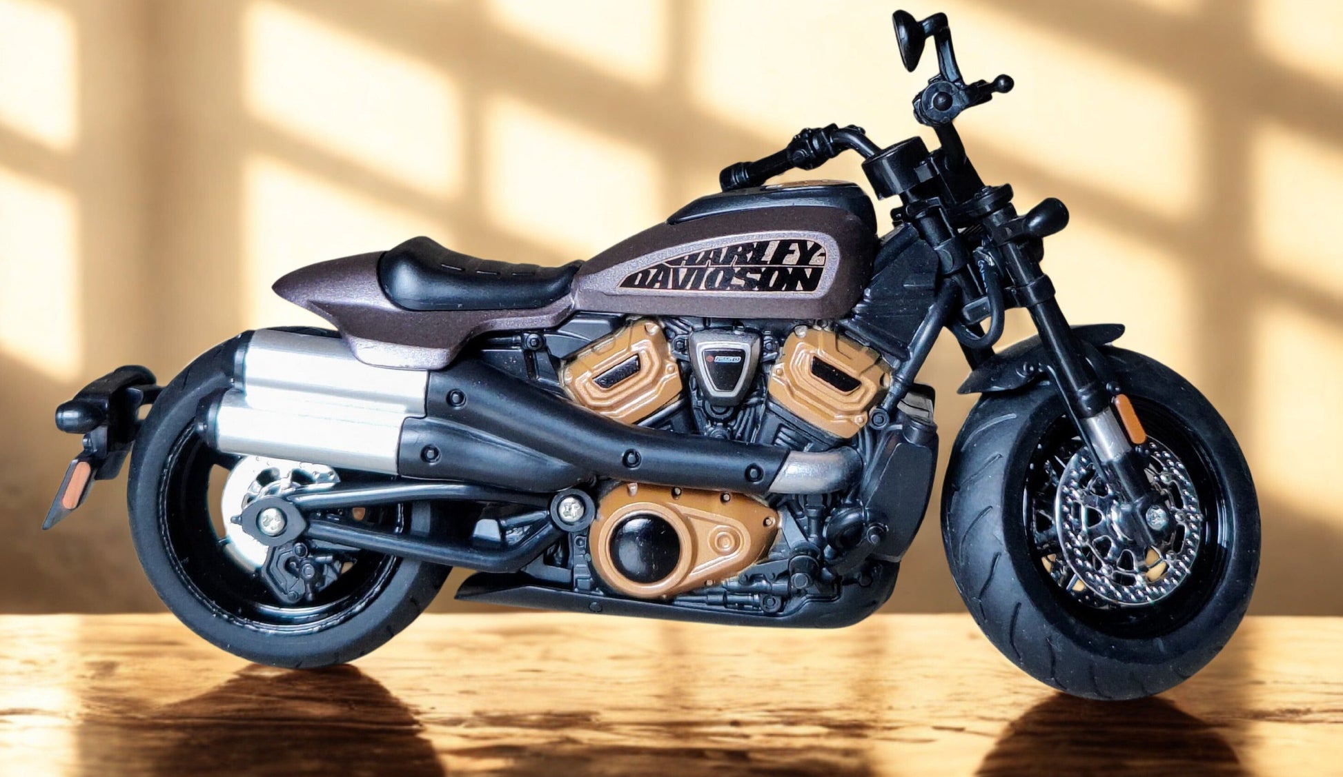 Diecast Harley-Davidson motorcycle model on a wooden floor with sunlight casting shadows.